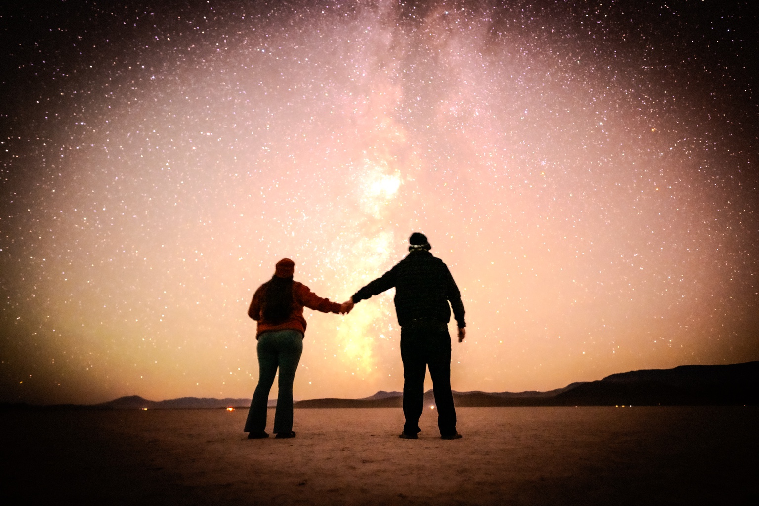 Two people holding hands under a glowing night sky