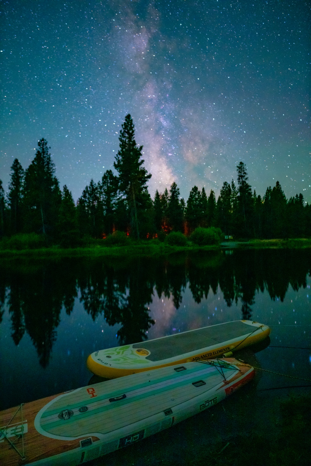 Paddleboards beneath a starry sky beside a forest lake