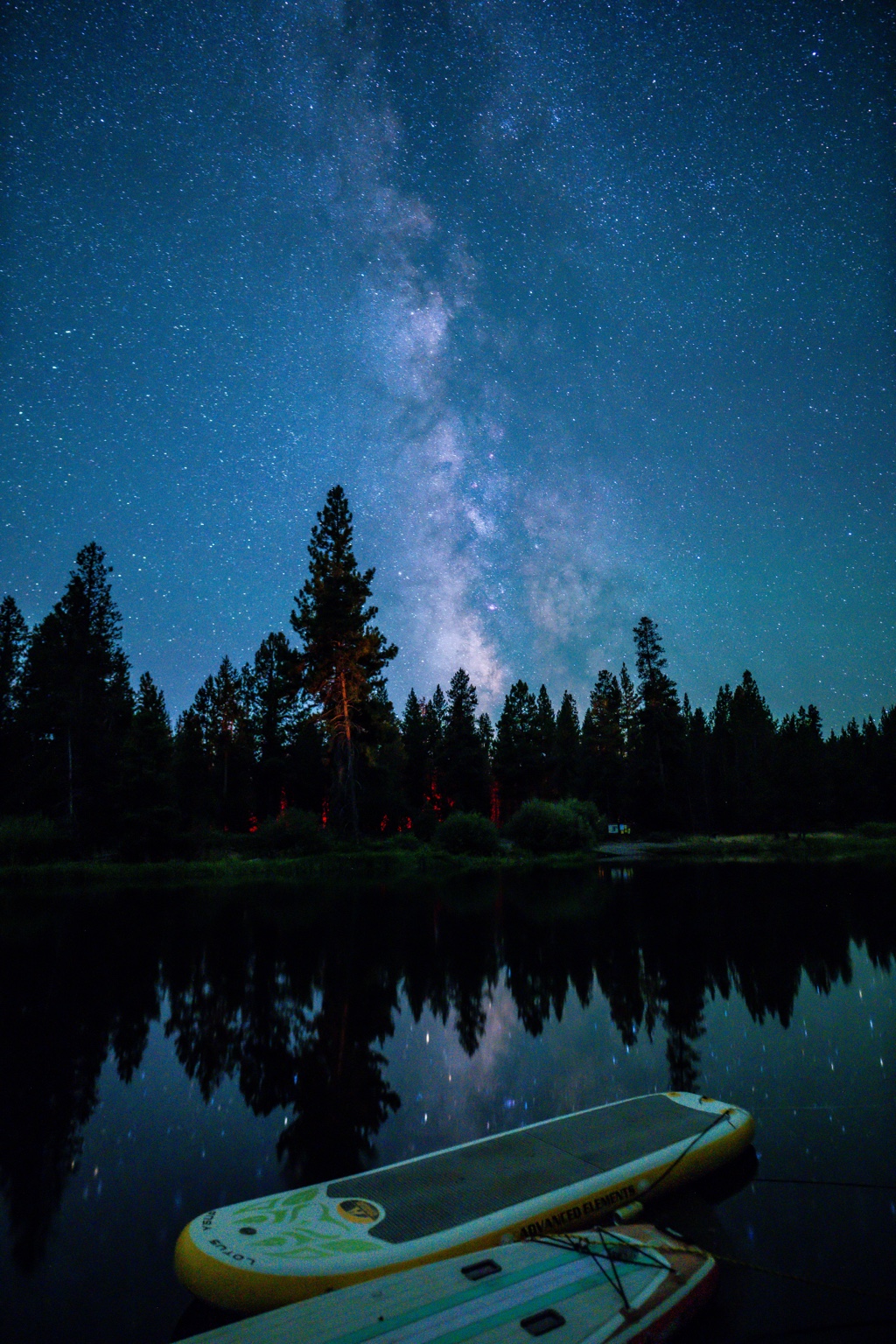 Paddleboards on a dark lakeshore with the Milky Way reflected in the water
